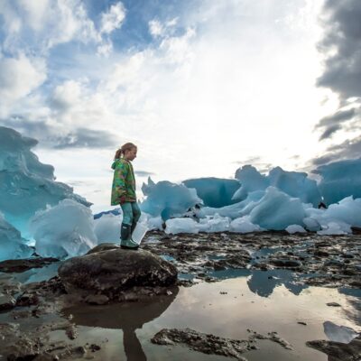 Child standing on a rock among beached icebergs from LeConte Glacier.